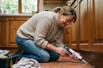 Femme en jeans et pull scellant une fissure dans la cuisine